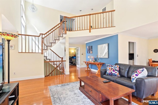 living area with stairs, a high ceiling, baseboards, light wood-style floors, and ornamental molding
