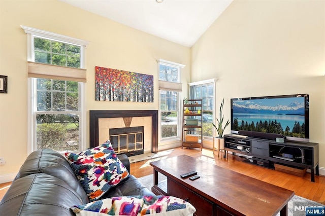 living room featuring baseboards, high vaulted ceiling, wood finished floors, and a tile fireplace