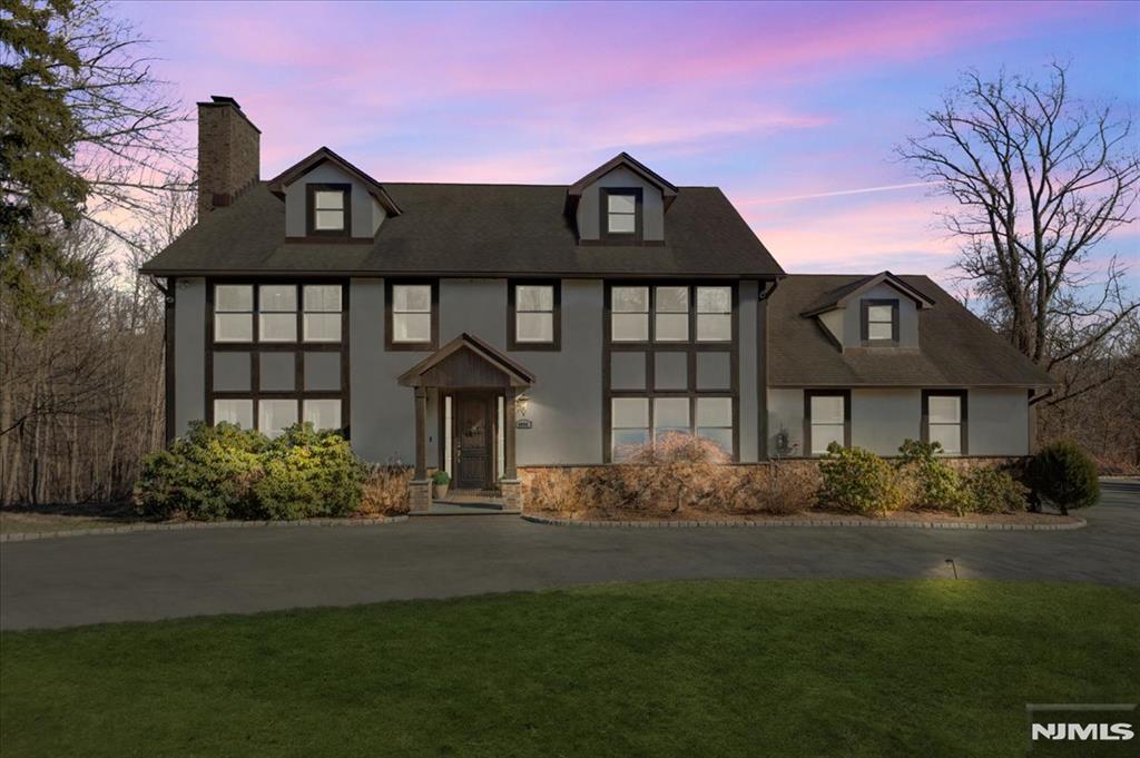 tudor-style house with a chimney, stucco siding, and a lawn