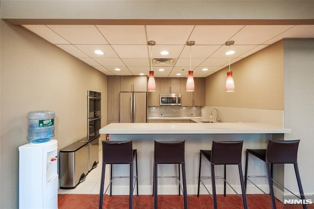 kitchen with a breakfast bar area, appliances with stainless steel finishes, a peninsula, visible vents, and decorative backsplash