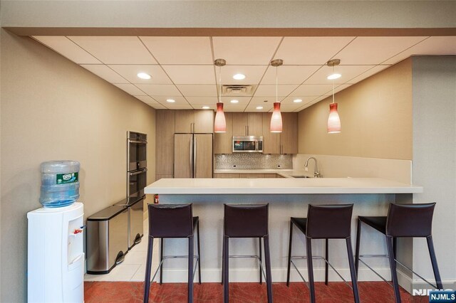 kitchen featuring a kitchen breakfast bar, appliances with stainless steel finishes, a peninsula, visible vents, and decorative backsplash