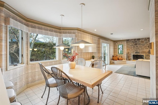 dining space with light tile patterned flooring, a stone fireplace, crown molding, and recessed lighting