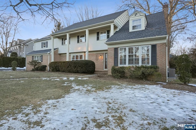 view of front of property featuring brick siding, central AC, roof with shingles, and a chimney