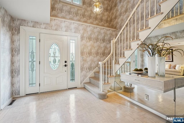 foyer entrance with baseboards, visible vents, a towering ceiling, and stairway