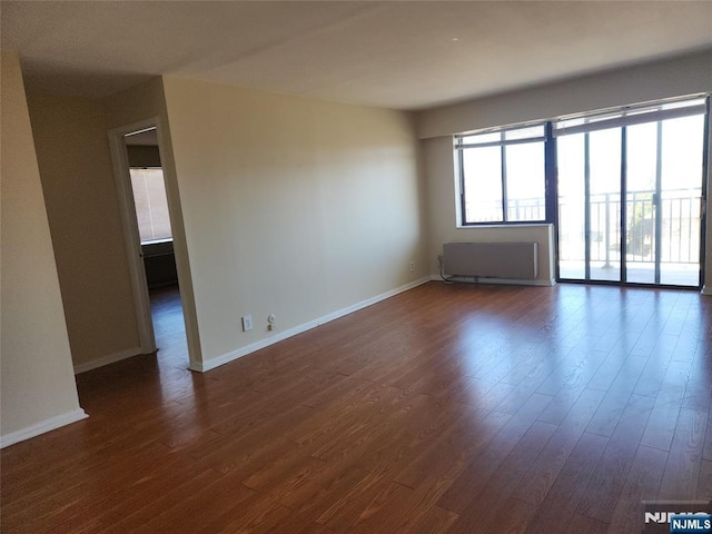 spare room with dark wood-type flooring, baseboards, and radiator