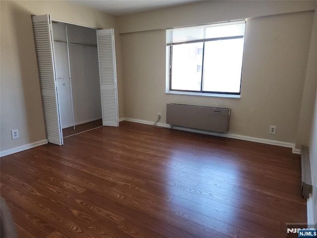 unfurnished bedroom with radiator heating unit, dark wood-style flooring, a closet, and baseboards