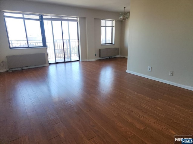 unfurnished room with an inviting chandelier, radiator heating unit, baseboards, and dark wood-type flooring