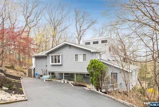 view of front facade featuring an outdoor structure, a shed, and aphalt driveway
