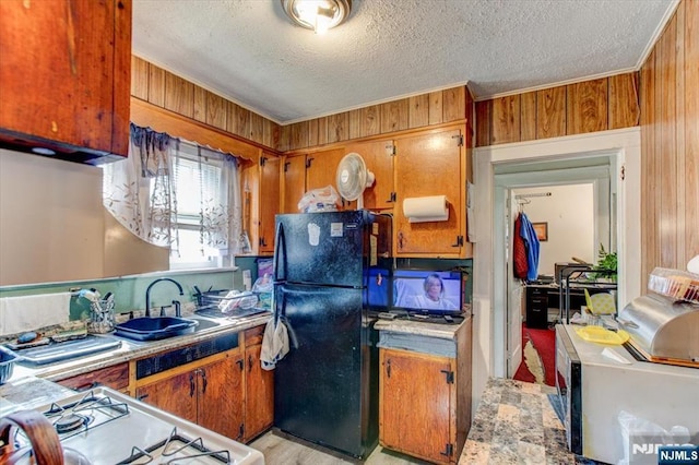 162 Summer St, Orange, NJ 07050 - kitchen featuring range with gas stovetop, wooden walls, freestanding refrigerator, brown cabinetry, and a sink