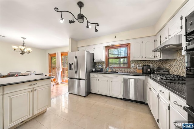 kitchen featuring dark countertops, appliances with stainless steel finishes, an inviting chandelier, backsplash, and under cabinet range hood