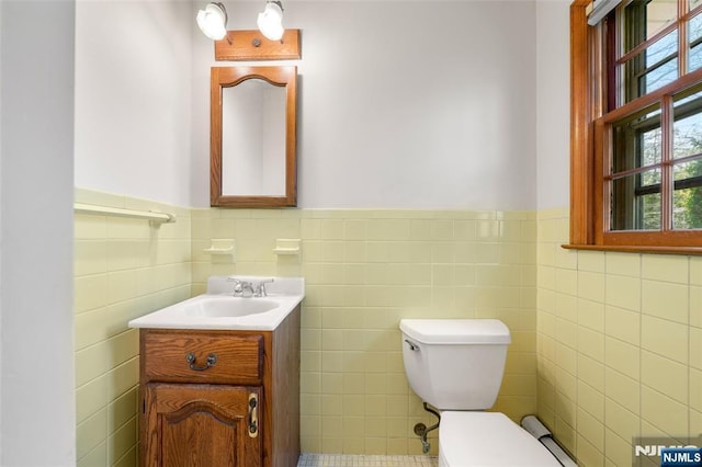 bathroom with plenty of natural light, a wainscoted wall, toilet, and tile walls