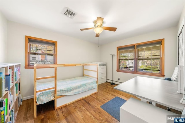 bedroom featuring baseboards, visible vents, wood finished floors, and a baseboard radiator