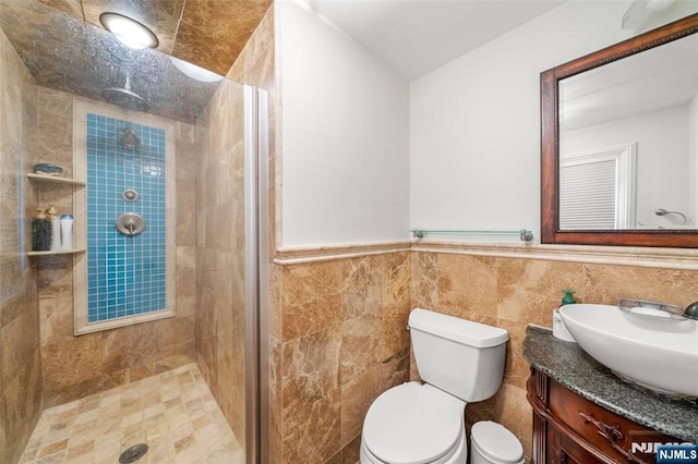 bathroom featuring vanity, wainscoting, toilet, and tiled shower