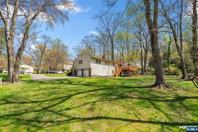 view of yard featuring a garage, a deck, driveway, and stairway