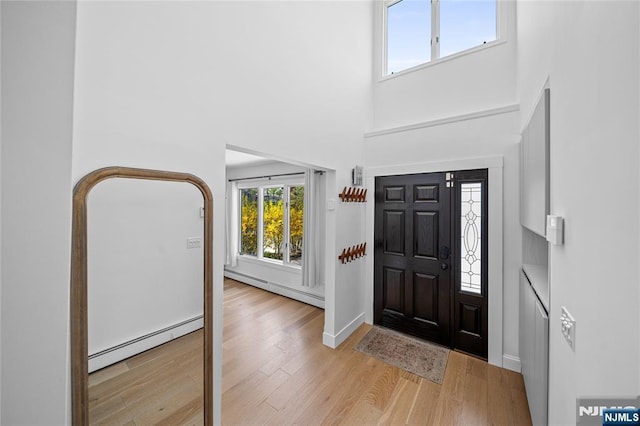 foyer featuring a baseboard radiator, baseboards, wood finished floors, a towering ceiling, and a baseboard heating unit