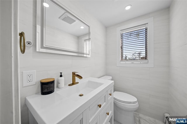 half bath featuring a healthy amount of sunlight, toilet, and tile walls