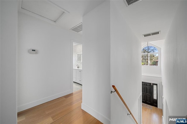 hall with visible vents, an upstairs landing, and light wood-type flooring