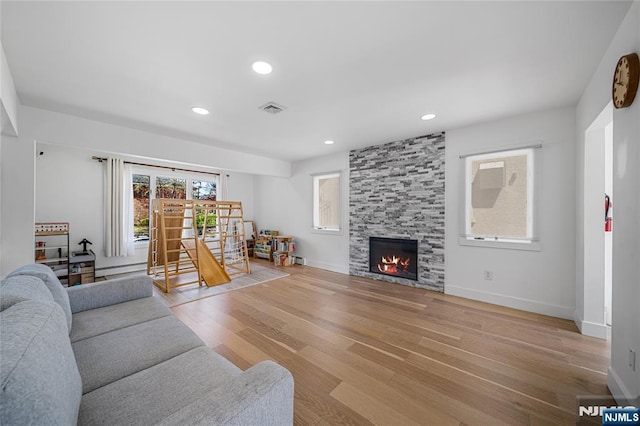 living area featuring visible vents, baseboards, recessed lighting, a large fireplace, and light wood-style flooring