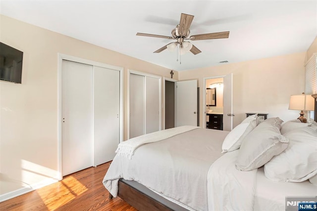 bedroom featuring multiple closets, wood finished floors, visible vents, connected bathroom, and ceiling fan