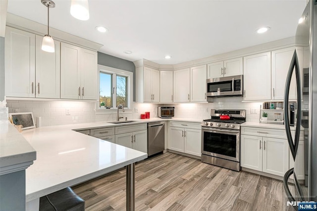 kitchen with a sink, light wood-type flooring, stainless steel appliances, backsplash, and a peninsula