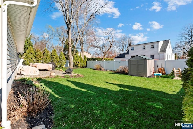 view of yard featuring a storage unit, an outbuilding, a fenced backyard, and an outdoor fire pit