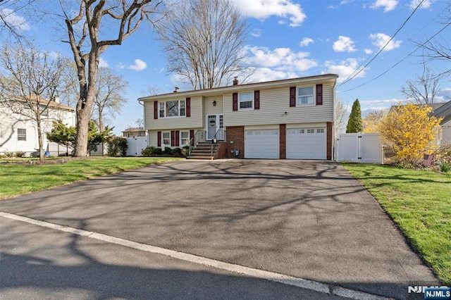 bi-level home with an attached garage, a front lawn, aphalt driveway, and a gate