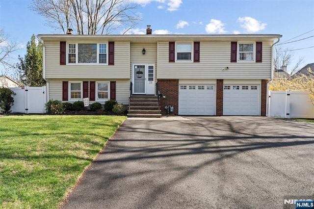 split foyer home with a gate, a front lawn, driveway, an attached garage, and fence