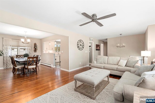 living room featuring ceiling fan with notable chandelier, baseboards, baseboard heating, and wood finished floors