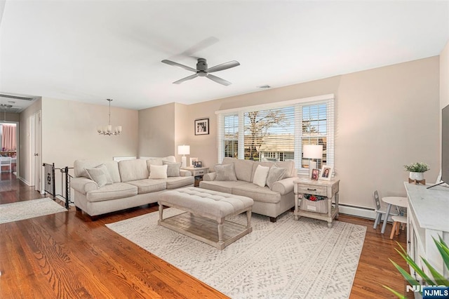 living area featuring a baseboard heating unit, baseboards, wood finished floors, and ceiling fan with notable chandelier