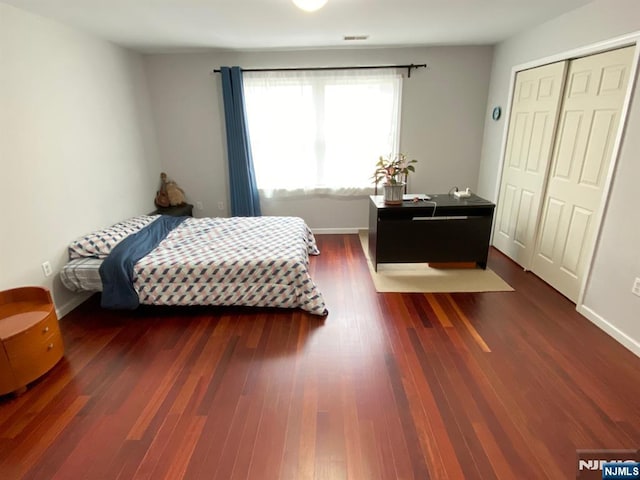 bedroom with dark wood-type flooring, a closet, and baseboards