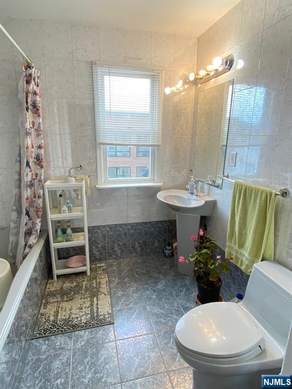 full bathroom with tiled shower / bath combo, tile walls, and toilet