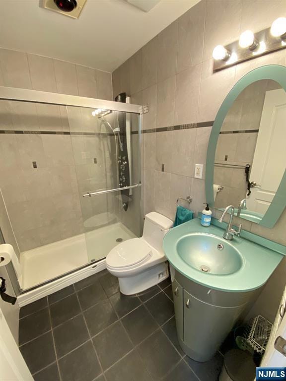 bathroom with vanity, tile patterned flooring, toilet, a shower stall, and tile walls