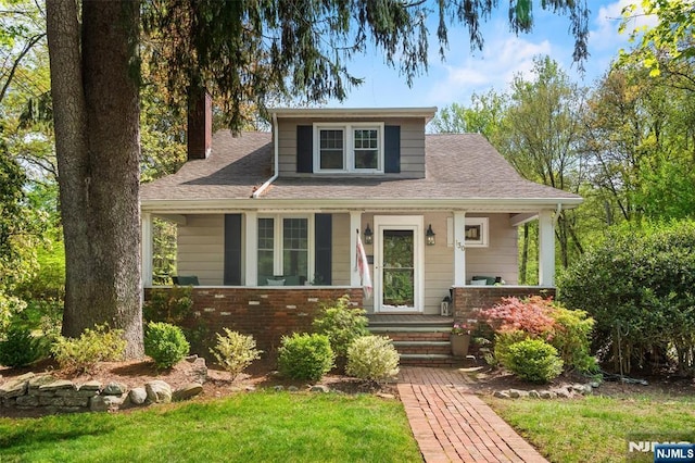 bungalow-style house with a front yard, roof with shingles, a chimney, brick siding, and a porch