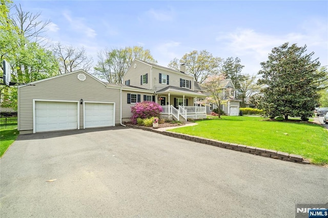 view of front of house featuring a front lawn, a garage, a chimney, covered porch, and driveway