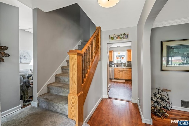 stairs featuring arched walkways, baseboards, visible vents, and wood finished floors