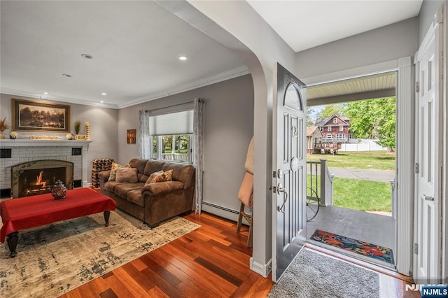 living area with plenty of natural light, a baseboard radiator, arched walkways, and wood finished floors