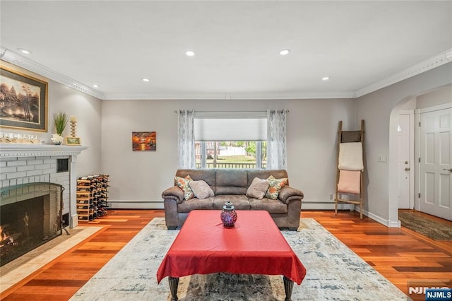 living area featuring crown molding, arched walkways, baseboard heating, and wood finished floors