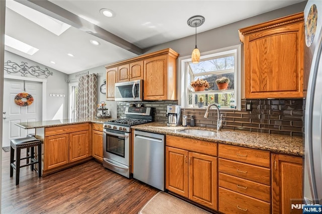 kitchen featuring appliances with stainless steel finishes, a sink, dark wood finished floors, a peninsula, and decorative backsplash