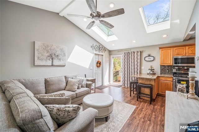 living area featuring a ceiling fan, a skylight, dark wood finished floors, high vaulted ceiling, and recessed lighting