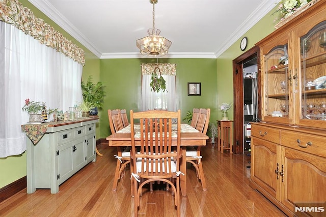 dining space with an inviting chandelier, crown molding, and light wood-style flooring