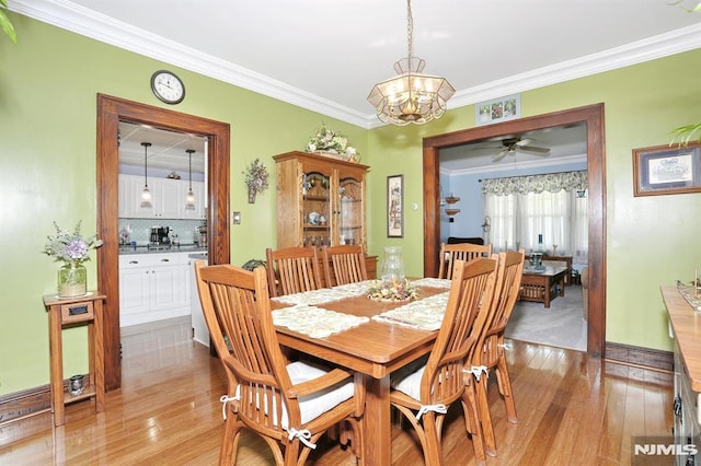 dining space with light wood-style flooring, ornamental molding, and ceiling fan with notable chandelier