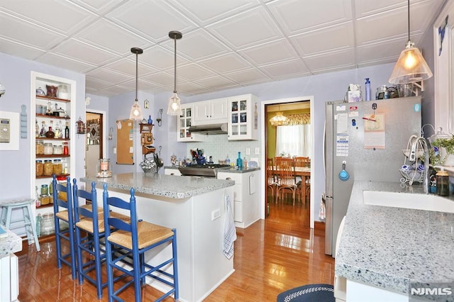kitchen with stove, white cabinets, under cabinet range hood, light wood-style floors, and a breakfast bar area