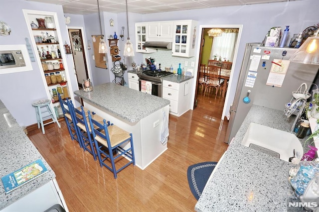 kitchen featuring white cabinets, light wood finished floors, stainless steel gas stove, a breakfast bar, and glass insert cabinets