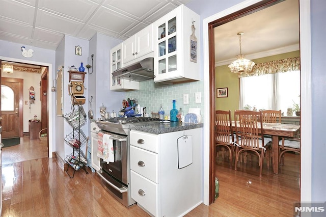 kitchen featuring stainless steel gas range, light wood-style floors, decorative backsplash, glass insert cabinets, and under cabinet range hood