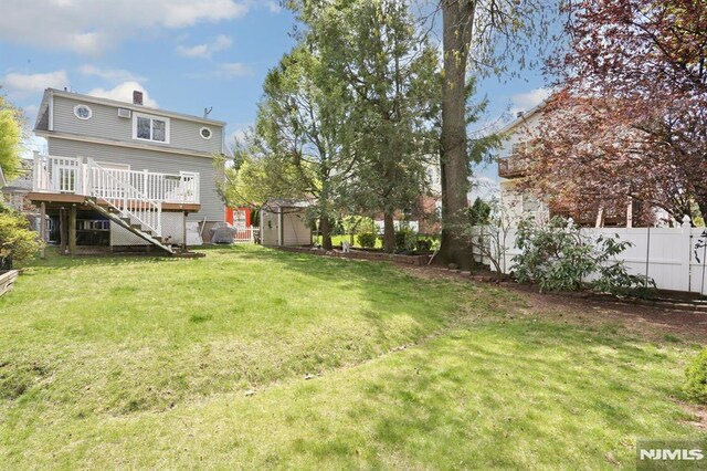 view of yard with fence, an outbuilding, a wooden deck, stairs, and a storage unit