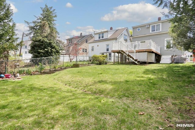 back of property featuring a lawn, a wooden deck, fence, and stairs