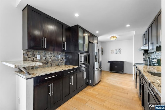 kitchen with decorative backsplash, light stone countertops, appliances with stainless steel finishes, under cabinet range hood, and light wood-style floors