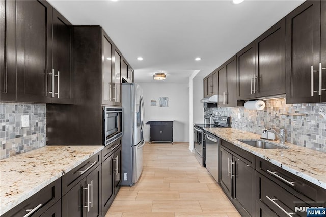 kitchen featuring a sink, light stone countertops, tasteful backsplash, appliances with stainless steel finishes, and under cabinet range hood