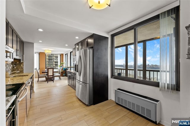 kitchen featuring radiator heating unit, stainless steel appliances, light wood-style floors, and ventilation hood
