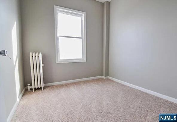 empty room featuring radiator, baseboards, and carpet flooring